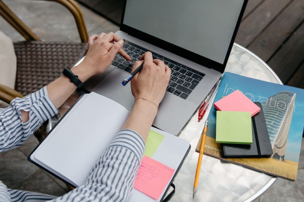Manos trabajando con un portatil, un cuaderno y notas
